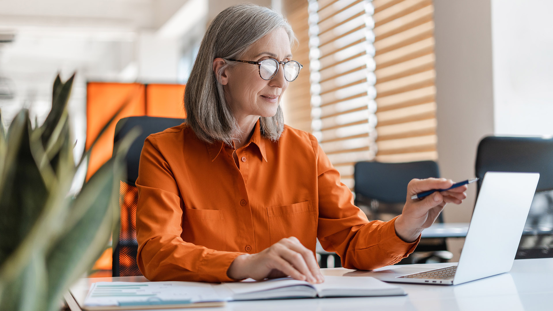 A person looking at a laptop screen in an office, with books and documents on the desk in front of them.